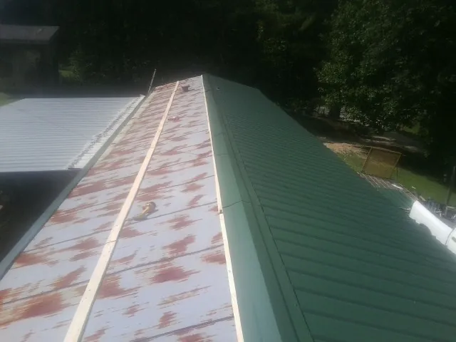 Old rusted panels beside newly installed green metal roofing — Wind Damage Roof Repair by Roofing Brothers in Hubbardston