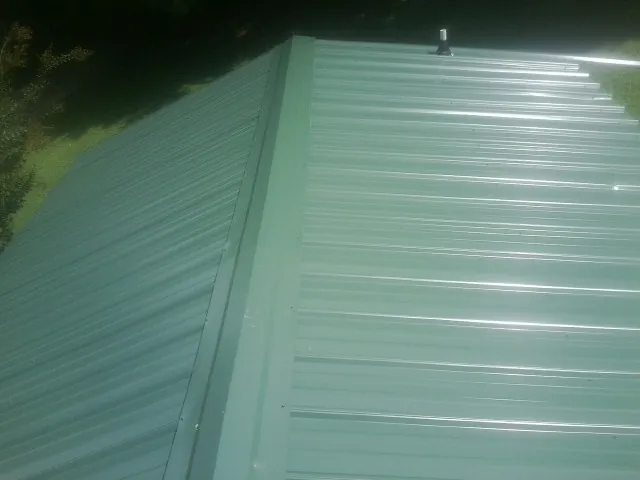 New green metal panels meeting at the ridge of a roof — Flat Roof Repair work by our crew in Hubbardston