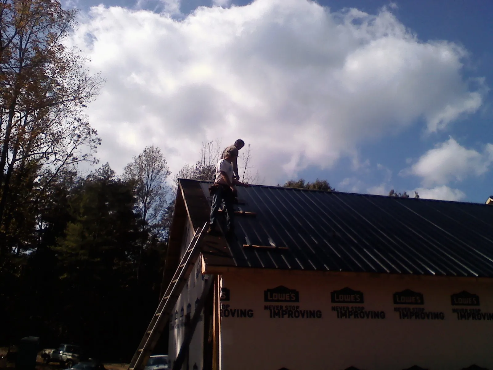 Roofer fastening dark metal panels high against a cloudy sky, from a Roof Inspection job in Hubbardston