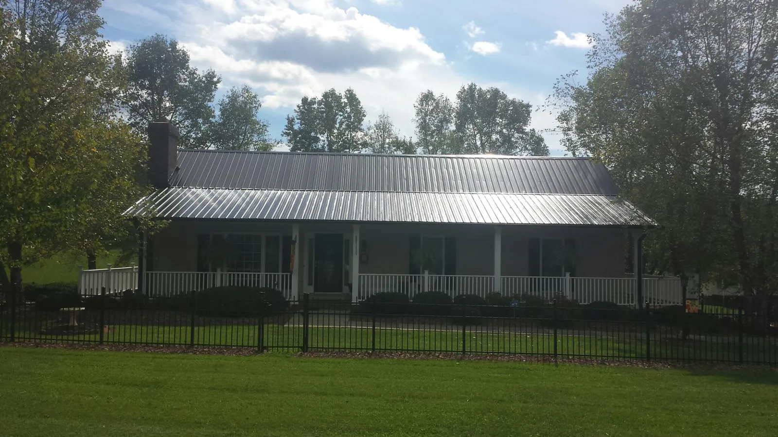 Gray metal roof on a brick ranch with a full width front porch — Gutter Guard Installation work by our crew in Hubbardston